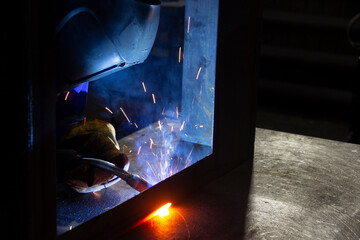 Manual metal welding, welding work in a mask, welding arc, sparks in the dark, bright flash of a welding arc, industrial welding in a protective suit, welding mask