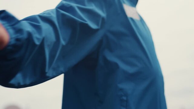 white man in blue jacket performing hand drills on urban rooftop during light rain, closeup sleeves and zipper details, windbreaker fluttering, rhythmic motion and gritty concentration