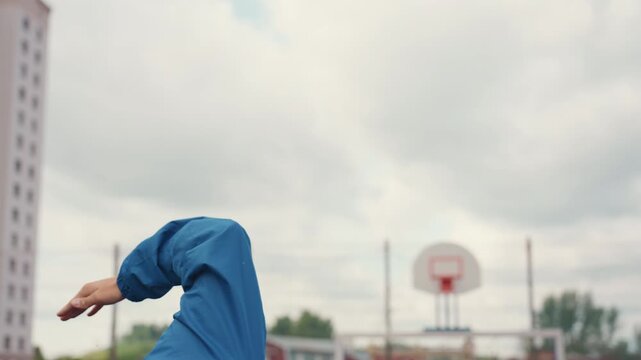white man in hooded blue jacket caught mid followthrough, arm extended and wrist rolled toward hoop, closeup detail of fingers and posture, cloudy sky and urban backboard visible, rainslick court