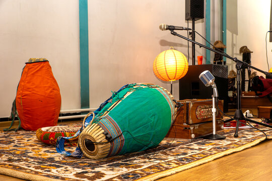 Instrument placement, mic stands, and floor seating confirm preparation for devotional chanting ensemble - ambient lighting supports focused performance and audience immersion with selective focus
