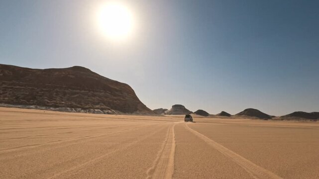 Distant following motion of jeep fast driving away across open white desert with sandy track under bright african sun