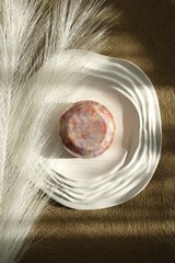 Flat Lay of Handmade Soap on White Plate with Feather and Sand. Eco-Friendly Skin Care Product.