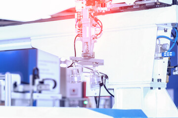 Disposable tableware manufacturing. An industrial robotic arm with suction cups holding plastic cups in a manufacturing environment. In the background is a blurred image of a factory environment