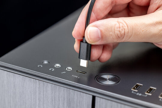A hand inserts a USB-C (aka Type-C) cable into the front port on a black metal desktop computer case. Close-up