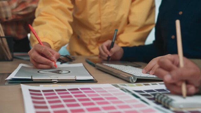 A vibrant workspace showcasing creativity and collaboration among designers, featuring hands engaged in brainstorming, sketches, and colorful palettes in a modern setting. SACTR