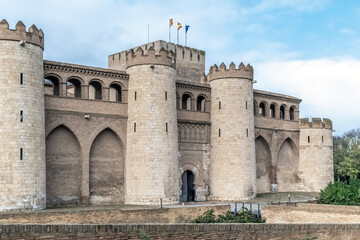Fototapeta premium Historical facade of Aljaferia Palace showing intricate Mudejar arches and round stone towers in Zaragoza. A prime example of Islamic architecture in Spain under a soft daylight sky