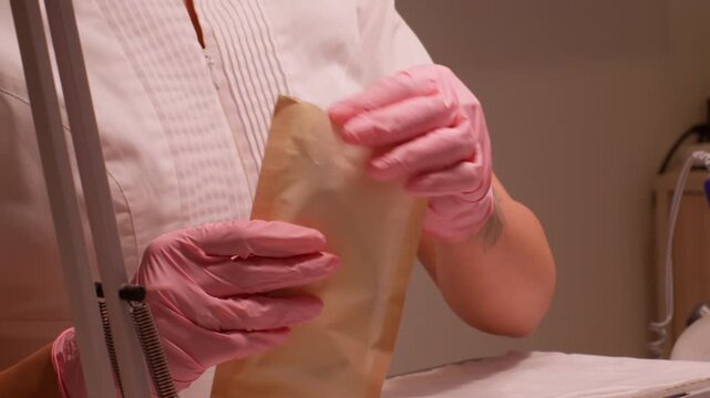 Salon sanitation. Nail hygiene. Beautician female hands in sterilized pink gloves taking tools forceps getting ready for beauty service care procedure.