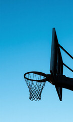 A silhouette of a basketball hoop against a clear blue sky, positioned on the right side of the image with open space on the left.