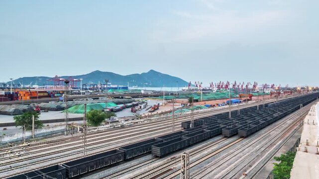 Time-lapse of a busy freight railway yard at nightfall, with cargo trains moving near a bustling port featuring cranes and shipping containers in Lianyungang, Jiangsu Province, China
