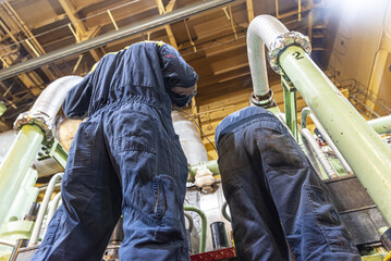 Marine engineers monitoring operating parameters of the main engine inside a ship engine room, industrial maritime maintenance work.