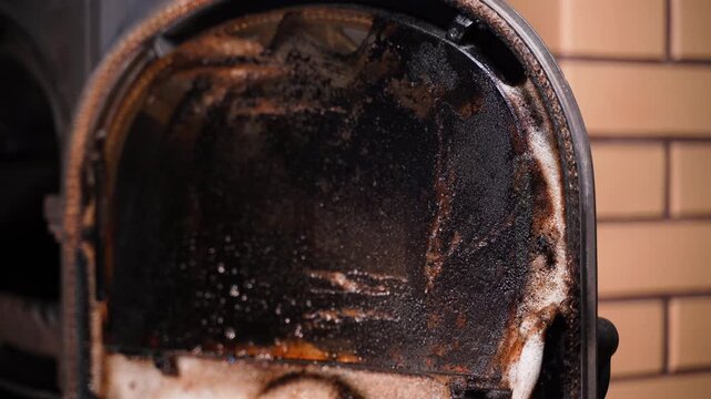 Spraying the fireplace stove window with detergent. Carbon and soot on the fireplace elements. Fireplace maintenance