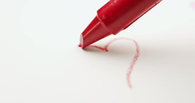 Red crayon drawing a small heart. Sketching a red heart showing love and kindness of a child through coloring. Childs drawing a heart for a loving Valentine's day, or a Father's or Mother's day card.