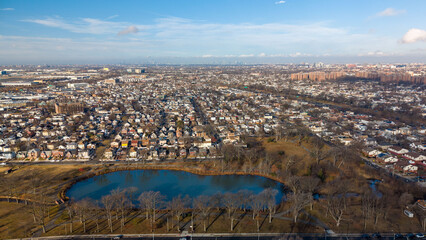 Obraz premium High angle view showing a residential neighborhood and sprawling city homes interspersed with a central park featuring a serene pond and bare winter trees