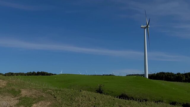 arge wind turbines on rolling green hills under a bright blue sky
