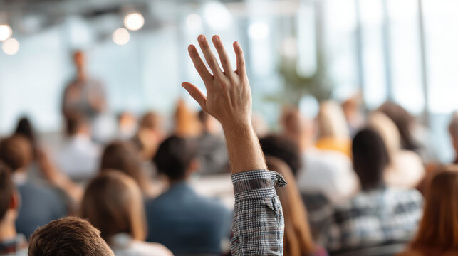 Meeting Question: A single hand raised high in a crowded conference setting. This photo captures the dynamic engagement within a corporate or academic assembly.