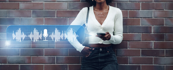 Woman stands against a wall using a smartphone with a voice recording feature displayed © fotofabrika