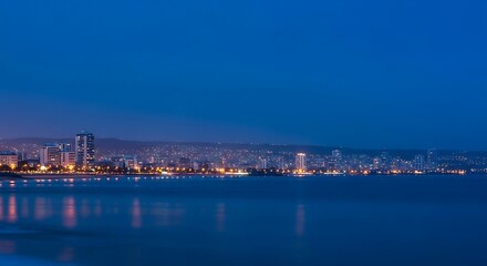 Obraz premium Serene Coastal City at Blue Hour with Soft Bokeh Lights Reflected in Calm Water | Peaceful Oceanfront Metropolis, Tranquil Evening