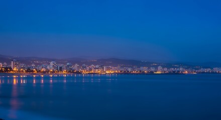 Obraz premium Serene Coastal City at Blue Hour with Soft Bokeh Lights Reflected in Calm Water | Peaceful Oceanfront Metropolis, Tranquil Evening