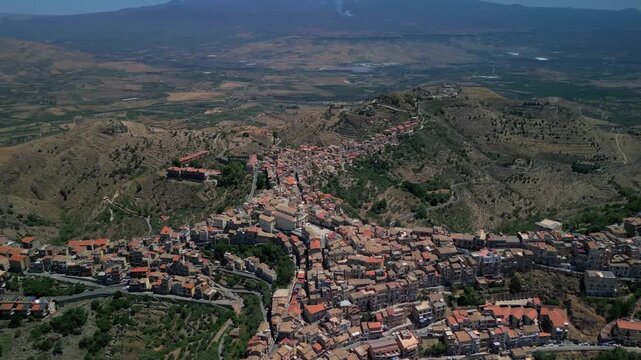 Atmospheric drone footage of Centuripe as sunset colors spread across the valley and Etna. Aerial view of Centuripe village glowing against darkening hills with Mount Etna behind.