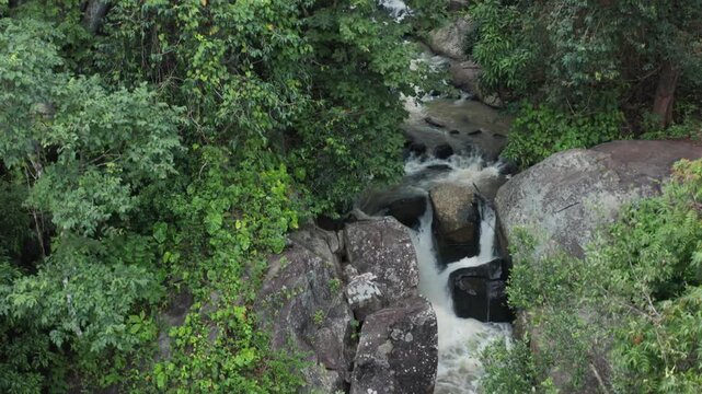 Dynamic aerial reveals multi-tiered Midubanda Waterfall gushing white foam over mossy rock ledges amid lush green vegetation and forested boulders near Daringbadi Odisha.