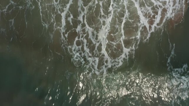 Top-down drone closeup showcases turbulent turquoise waves foaming and swirling across Kuity Beach waters in Odisha's coastal haze.