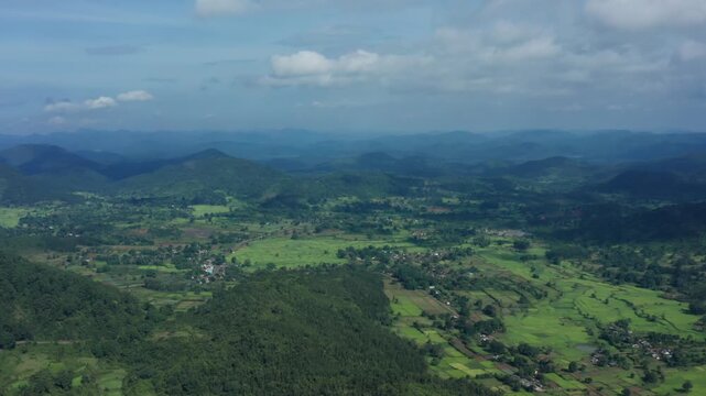 Vast aerial panorama of Daringbadi's rolling green hills dotted with terraced paddy fields, small villages, dense forests, and distant blue ridges under partly cloudy skies Odisha.
