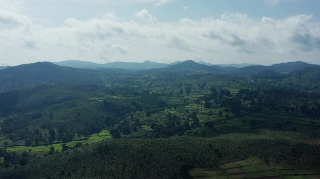 Aerial sweep of Daringbadi's rolling green hills, terraced fields, and forested valleys in Odisha's Kashmir-like landscape under partly cloudy skies.