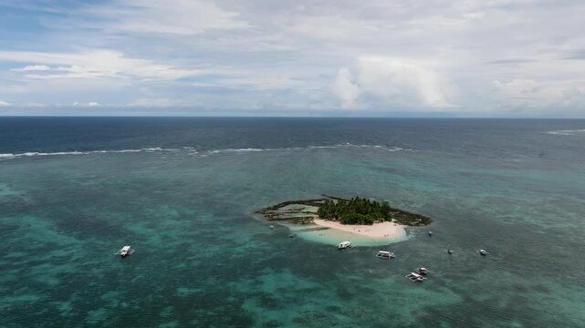 Tourist boats anchored close to a sandy tropical island with palm trees. Guyam Island. Siargao, Philippines.
