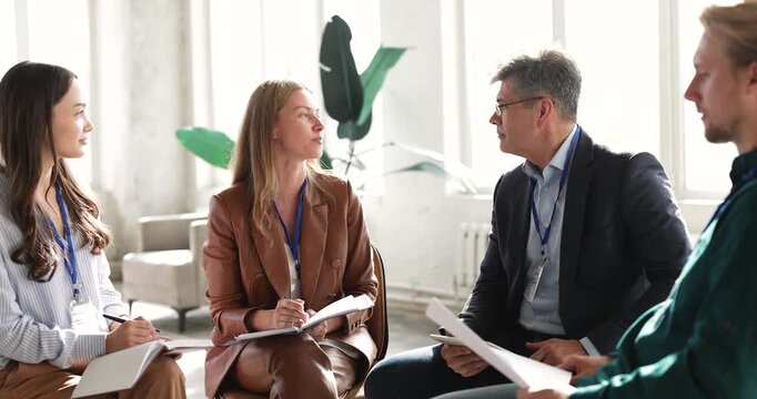 Female professional leading team discussion, explaining ideas, providing information or point to diverse colleagues seated in circle in modern office. Teamwork, leadership, coaching, business