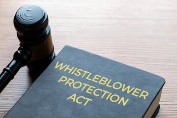 A judge's gavel and a book titled WHISTLEBLOWER PROTECTION ACT on a wooden desk surface. Justice...