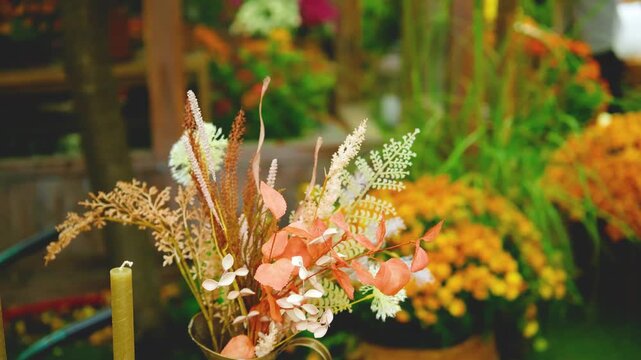 Dried flowers and green plants in a vase with candles in a soft focus garden setting