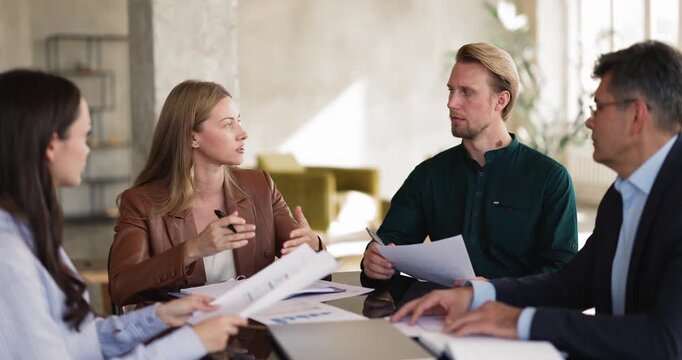 Female team leader explains business strategy, guides colleagues through project details during corporate meeting, group reviewing documents, analyzing data, collaborates on decision making in office