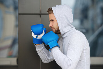 Strong boxer in sportswear. Exercising and punching. Practicing boxing. Sportsman boxing gloves outdoor. Young man boxer. Sport man boxing. Strong athlete man. Sportsman in hoodie. Sparring session