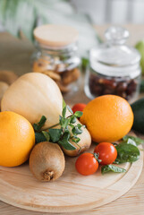 A vibrant collection of fresh produce including oranges, kiwi, butternut squash, tomatoes, and spinach, arranged on a wooden board with jars in the background