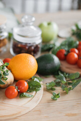 A vibrant assortment of fresh fruits and vegetables including an orange, avocado, tomatoes, and herbs are artfully arranged on a rustic wooden surface