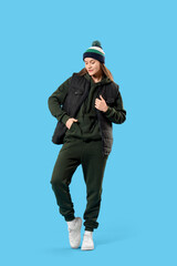 Naklejka premium Young woman in sports suit with warm hat on blue background