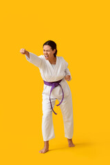 Young African-American woman practicing karate on yellow background
