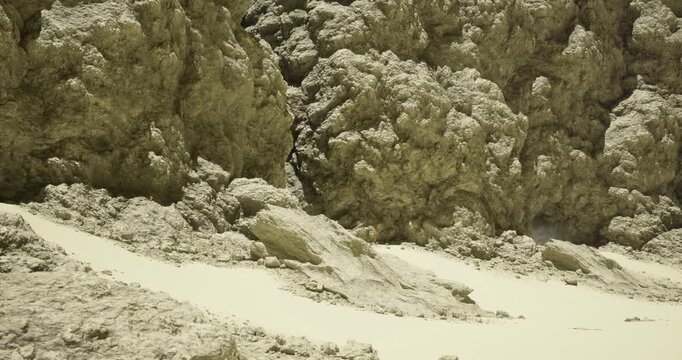 A rugged and dry landscape characterized by large, bold rock formations. The rocky surface features sharp textures and varying shades of color under bright daylight.