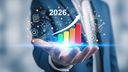 A businessman holding a glowing bar graph with icons and a target year of 2026 in his hand.
