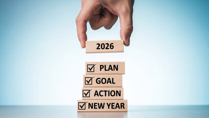 A hand placing a block with the year 2026 on top of blocks with the words plan, goal, action, and new year.