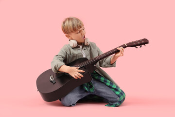 Fototapeta premium Little boy playing guitar on pink background