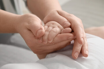 Mother holding her little baby's hand at home, closeup