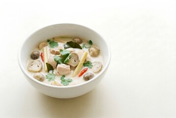 Tom Kha Gai in white bowl. Authentic coconut milk soup with chicken, mushroom and herb for dinner. Asian food, healthy cuisine.