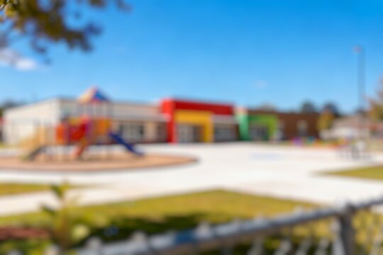 Defocused colorful kindergarten playground with rubber flooring and play structures under clear blue sky
