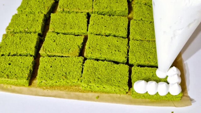 Decorating green matcha sponge cake with white cream piping for layer assembly