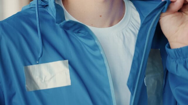 white male zipping blue jacket, fastening reflective tape panels and collar, closeup of hands and zipper revealing white tee, sequence evokes courier prepping for shift, commuter adjusting gear,