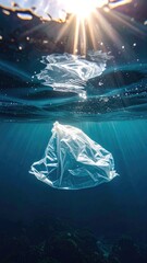Obraz premium A plastic bag floats suspended in deep blue ocean water beneath bright sunrays piercing the surface.