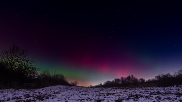 Vivid aurora borealis illuminating the winter night sky above snow-covered open field in Silesia region of Poland, with intense green and magenta light pillars, 19.01.2026