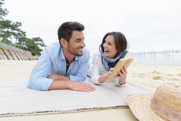 Obraz premium couple layed on the sand laughing at contents of book