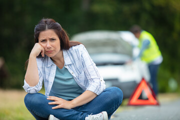 woman sitting near warning triangle and broken car on road